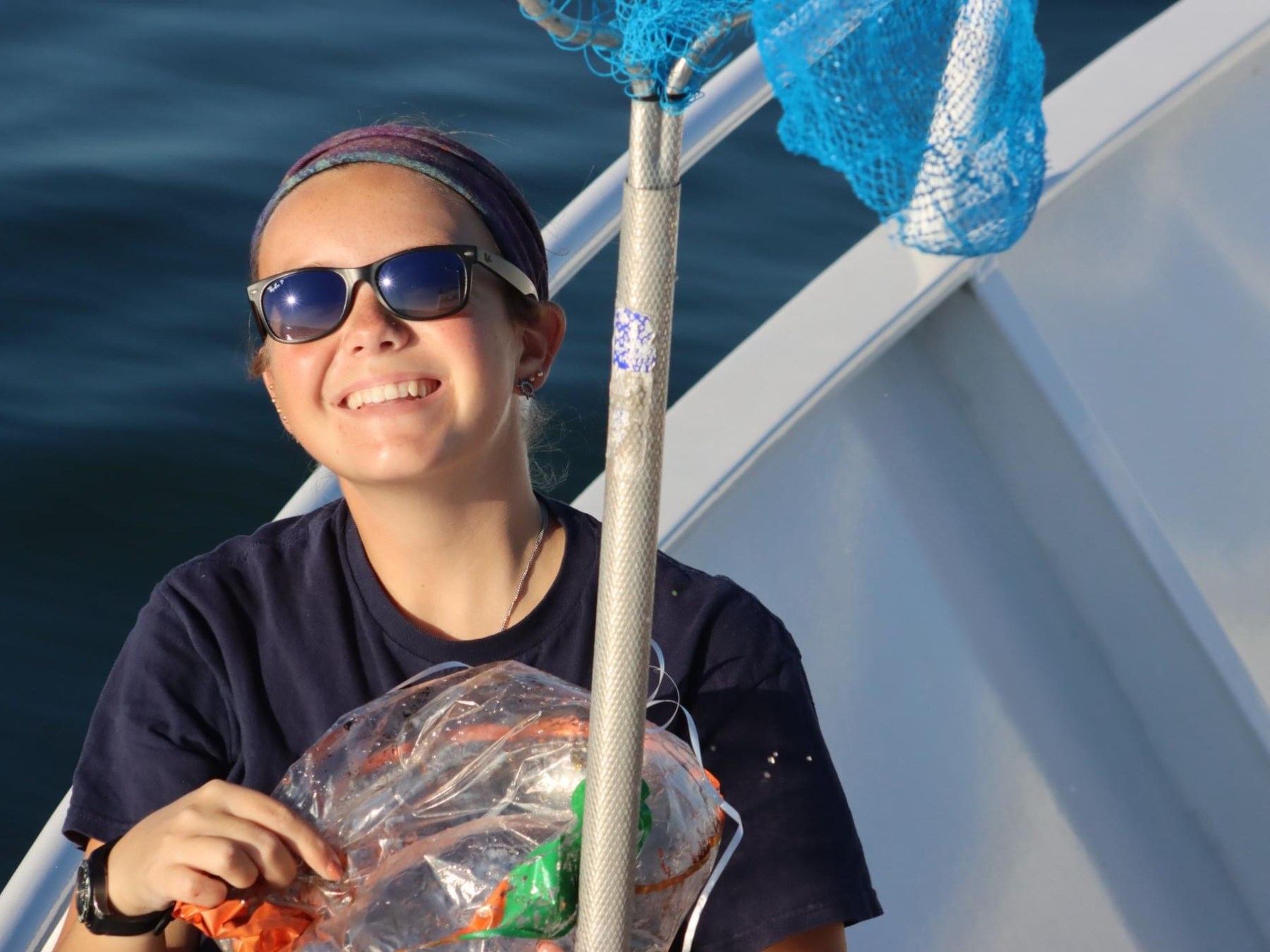 Person on a boat, wearing sunglasses, holding a net and smiling.