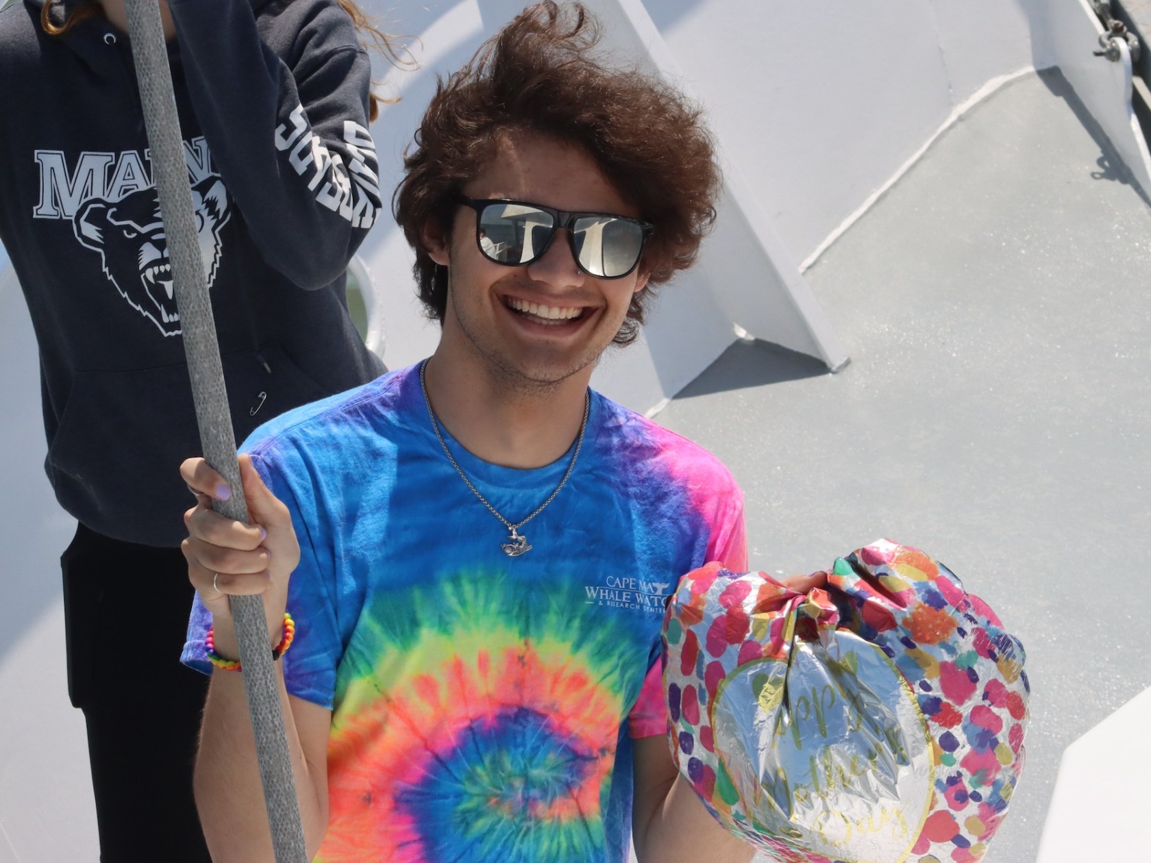Smiling person in tie-dye shirt holding colorful balloon on a boat.
