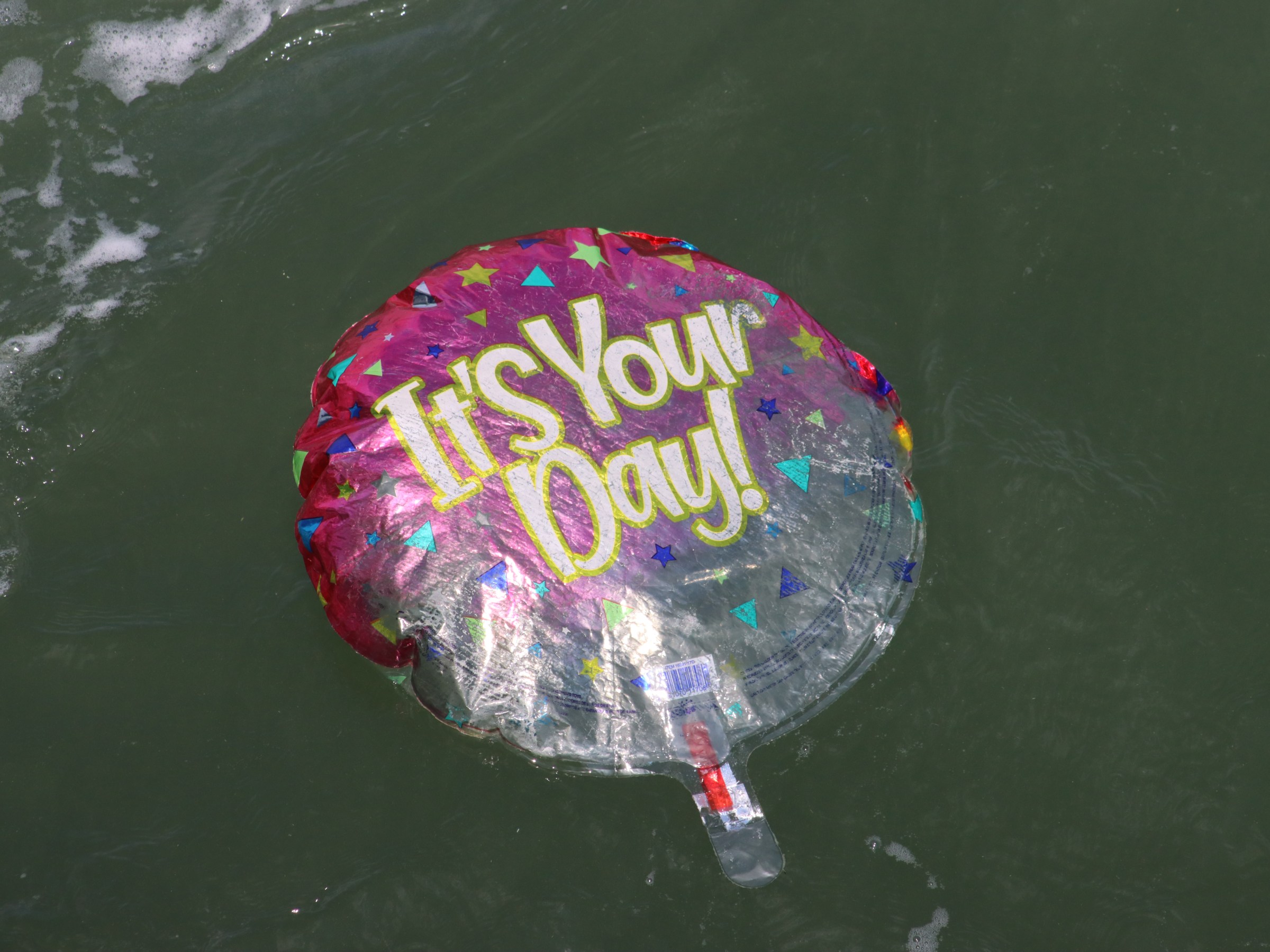 Deflated balloon with 'It's Your Day!' floats on water surface.