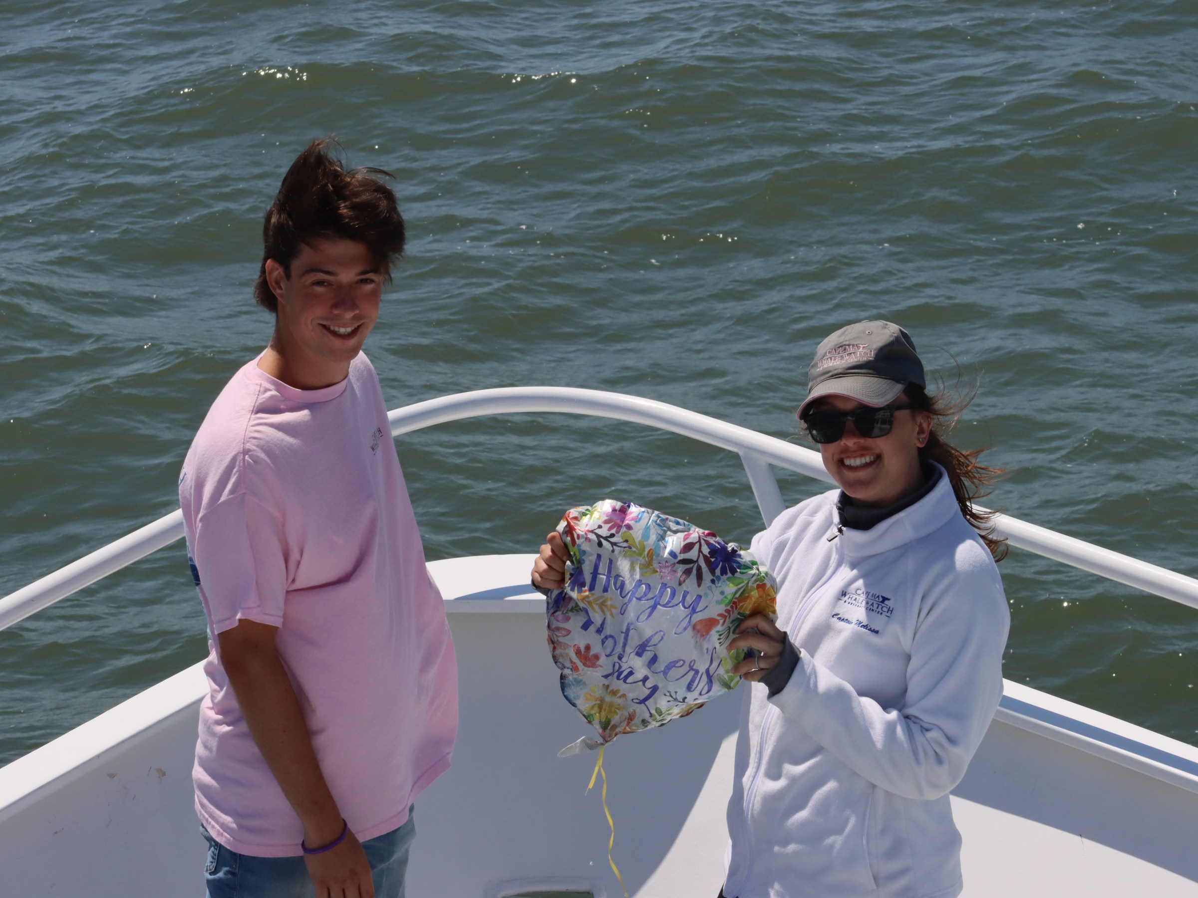 Two people on a boat holding a 'Happy Mother's Day' balloon with water in the background.