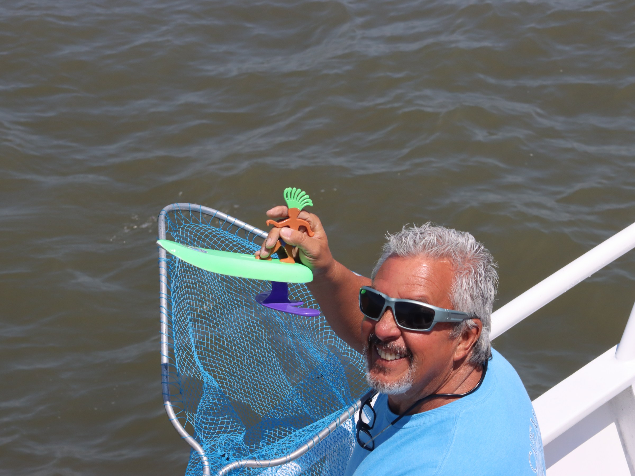 Man on a boat holding a fishing net with a green and purple object.