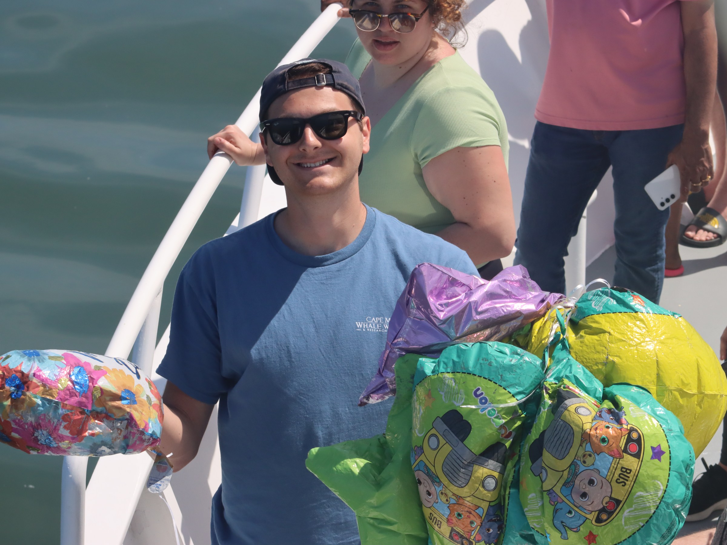 Person in blue shirt holding colorful balloons on a boat with other people.