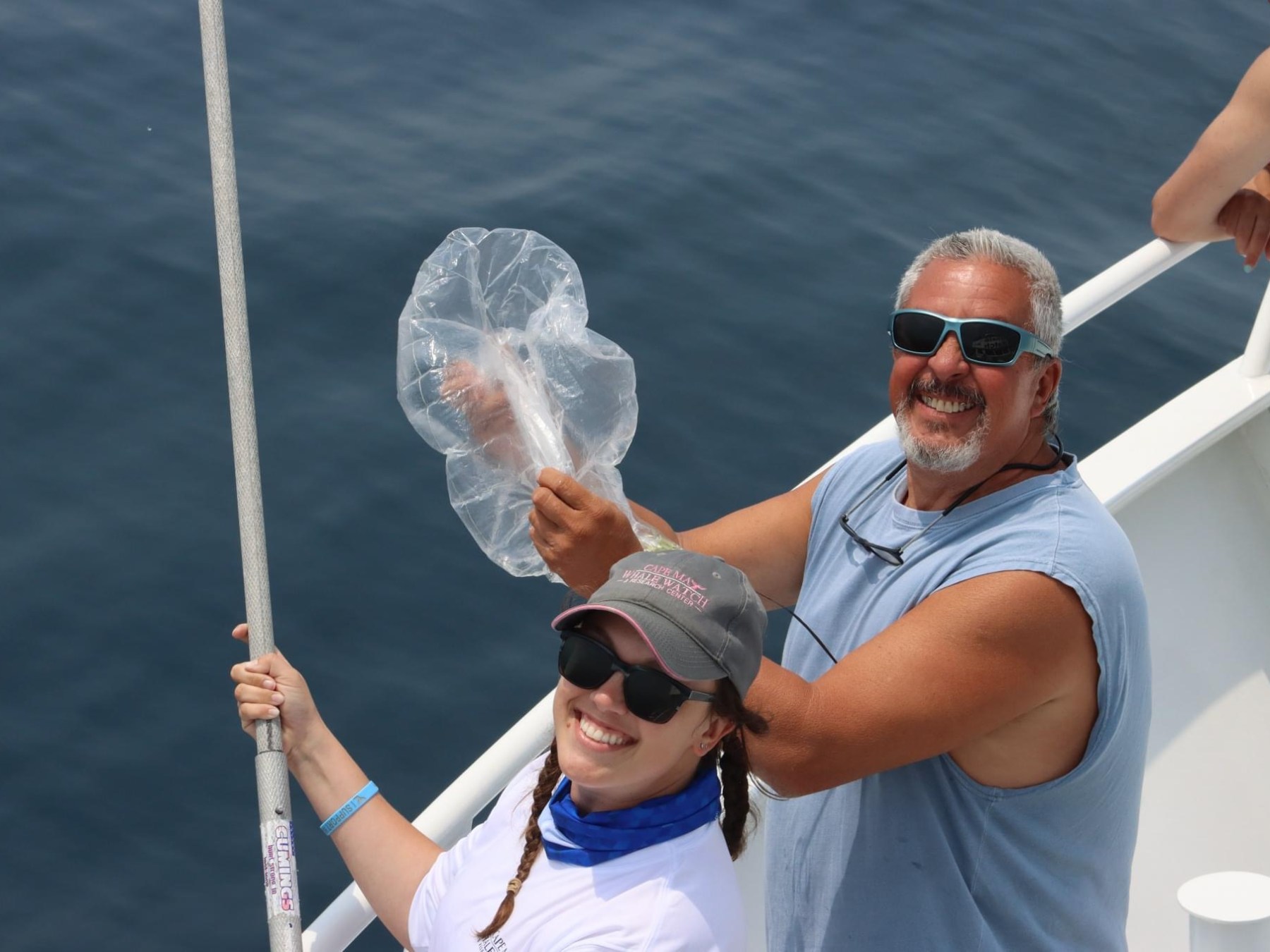 Two people on a boat, smiling and holding a pufferfish with a net pole.