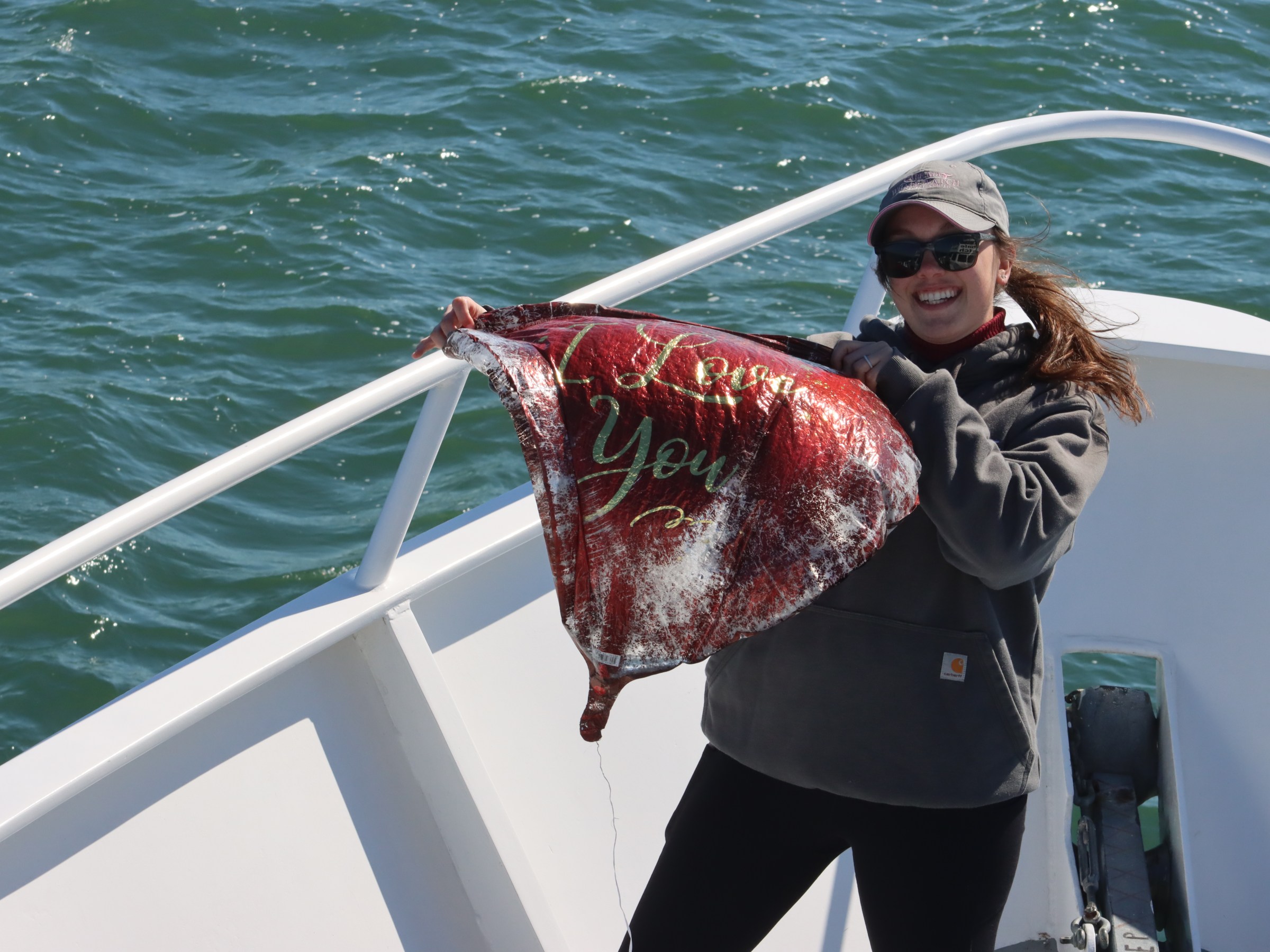 Person on a boat holding a deflated 'I Love You' balloon over the water.