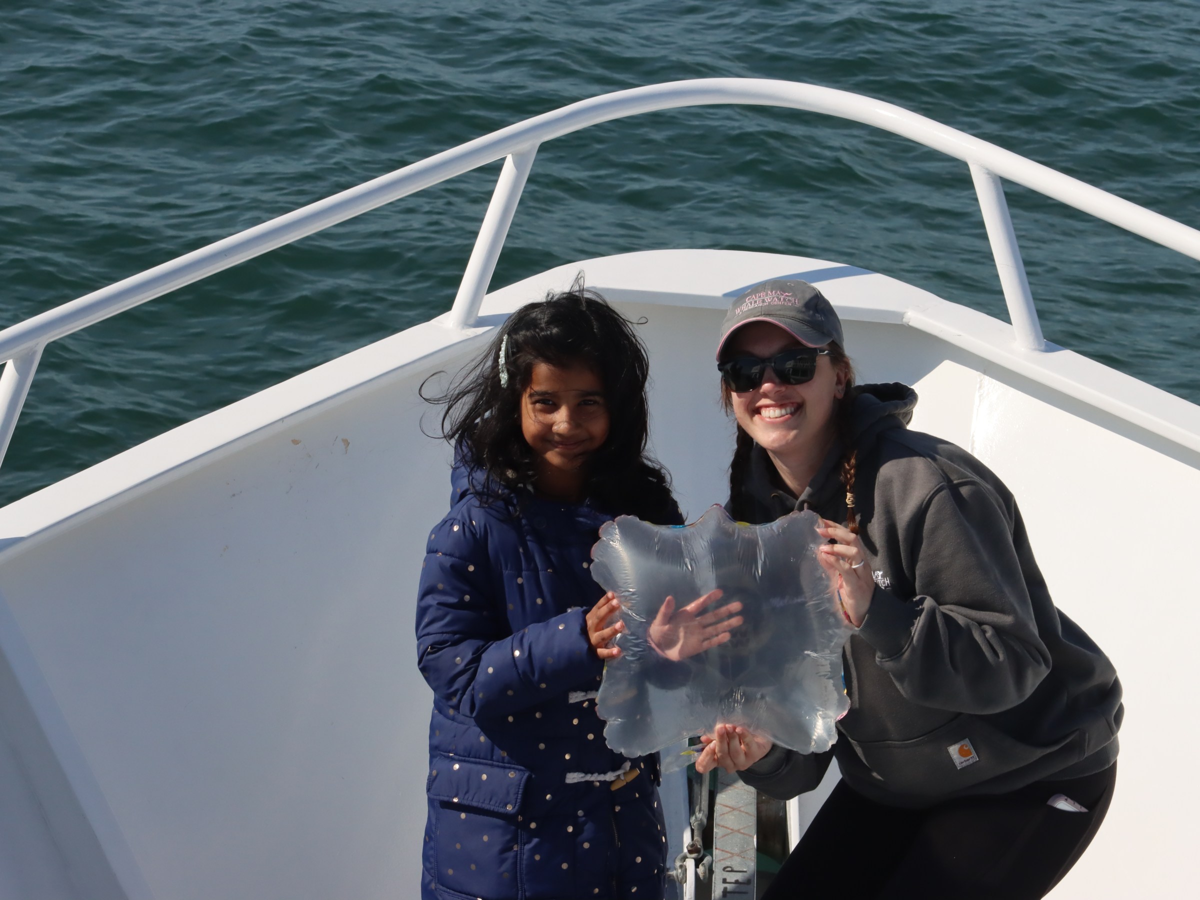 Two people on a boat holding a large, translucent sea creature.