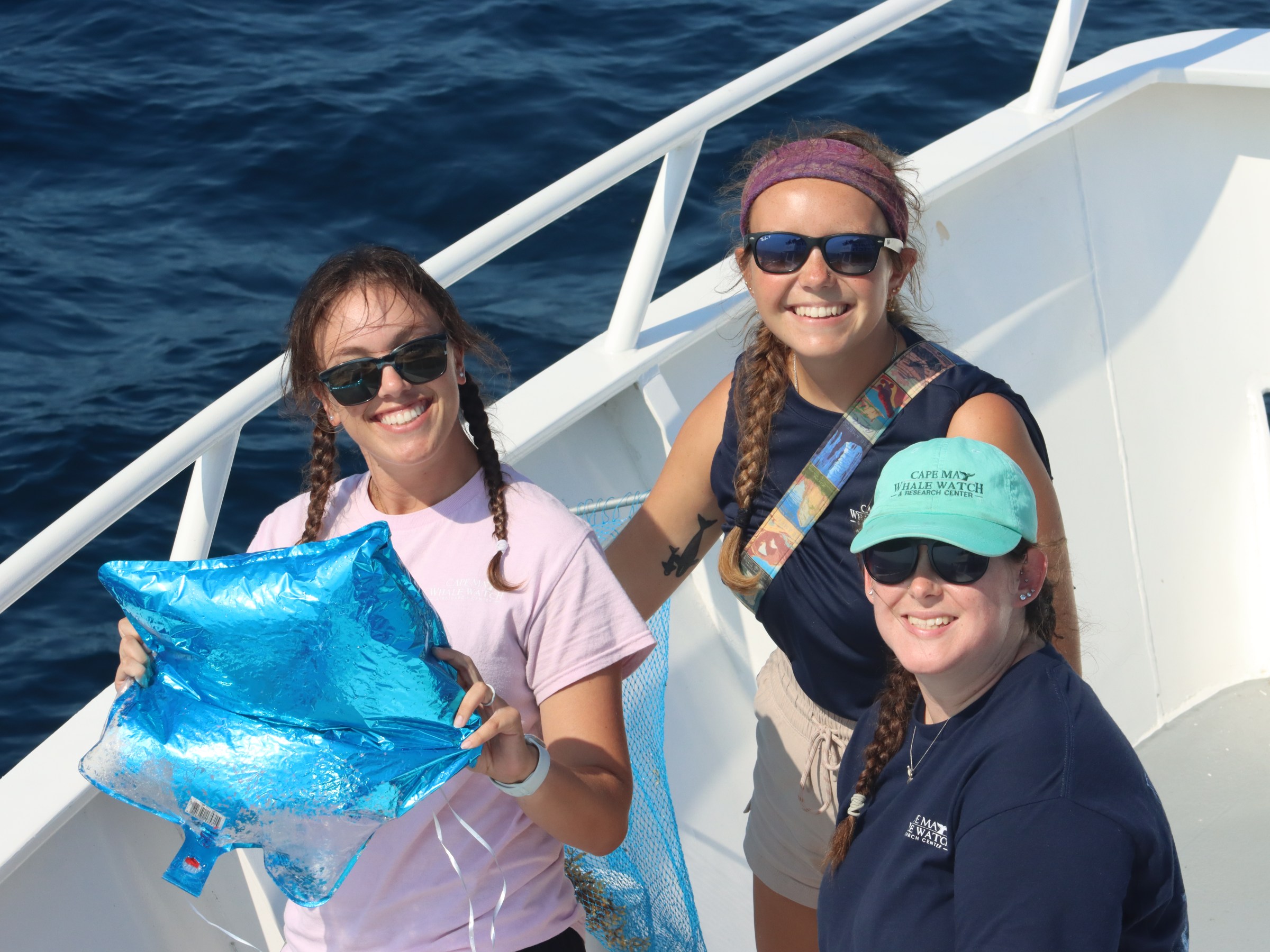 Three people on a boat holding a deflated blue balloon and a net.