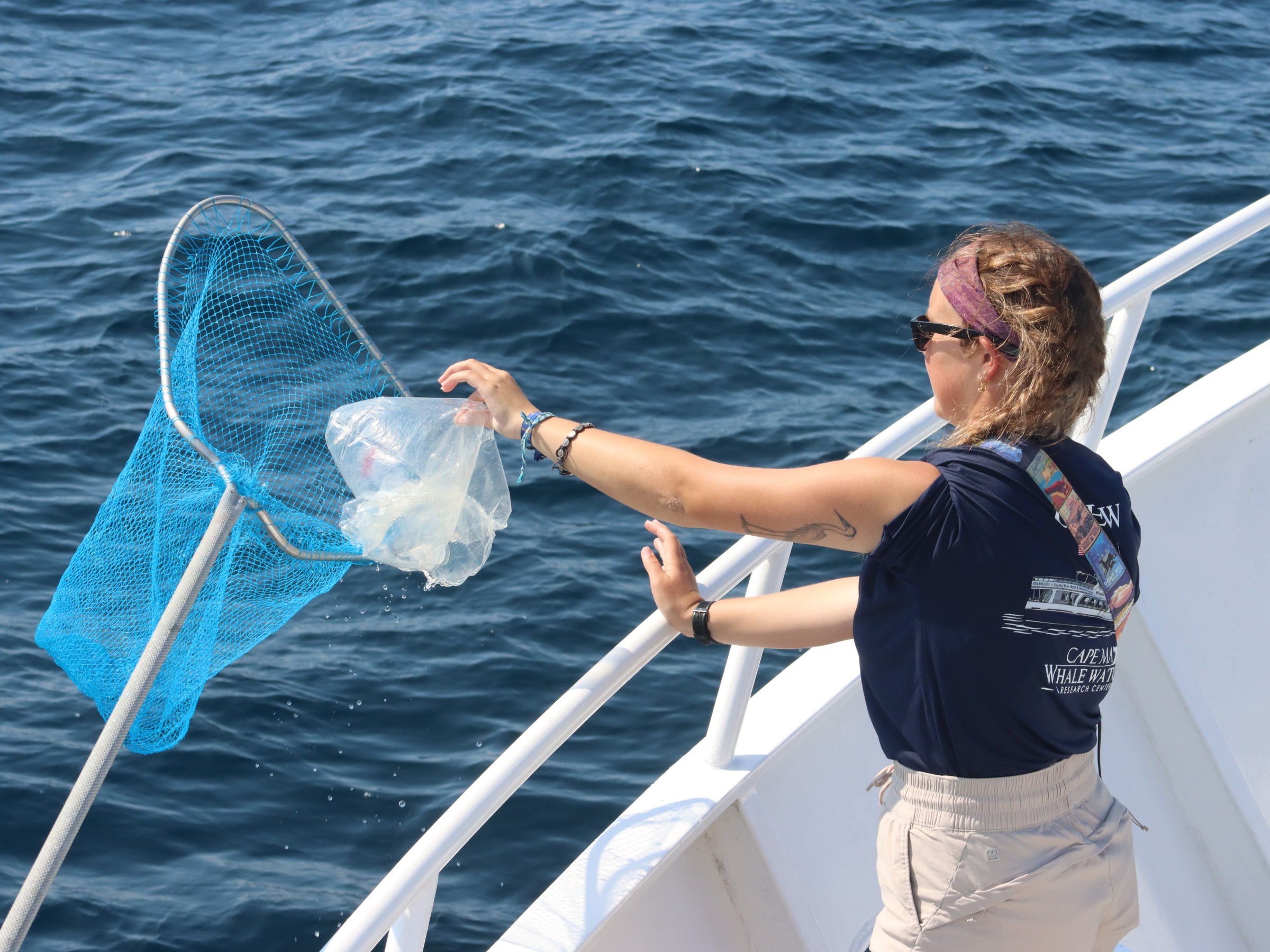 Woman on boat collecting plastic from ocean with a net.
