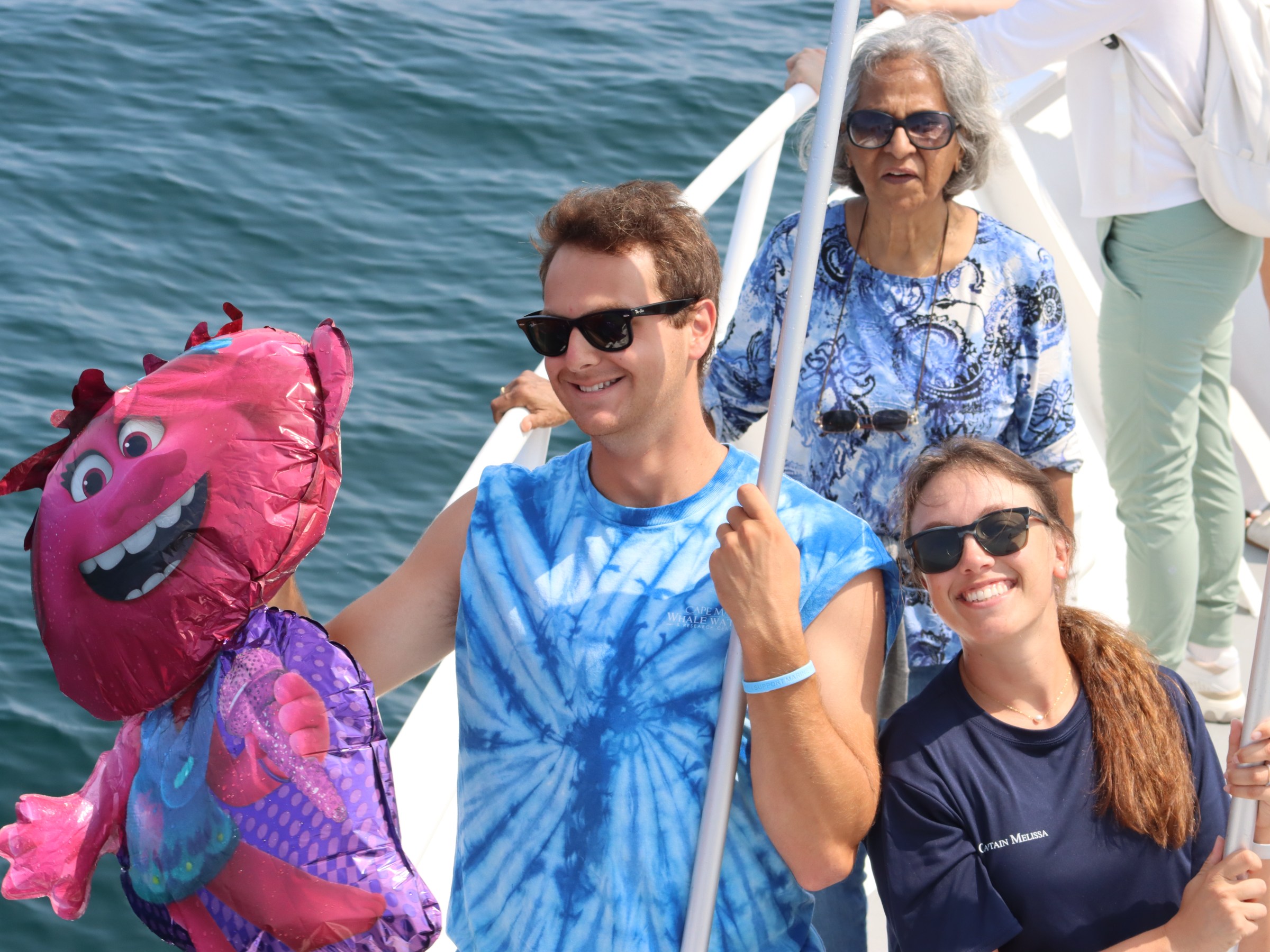 Two people holding a pink cartoon balloon on a boat with ocean background.