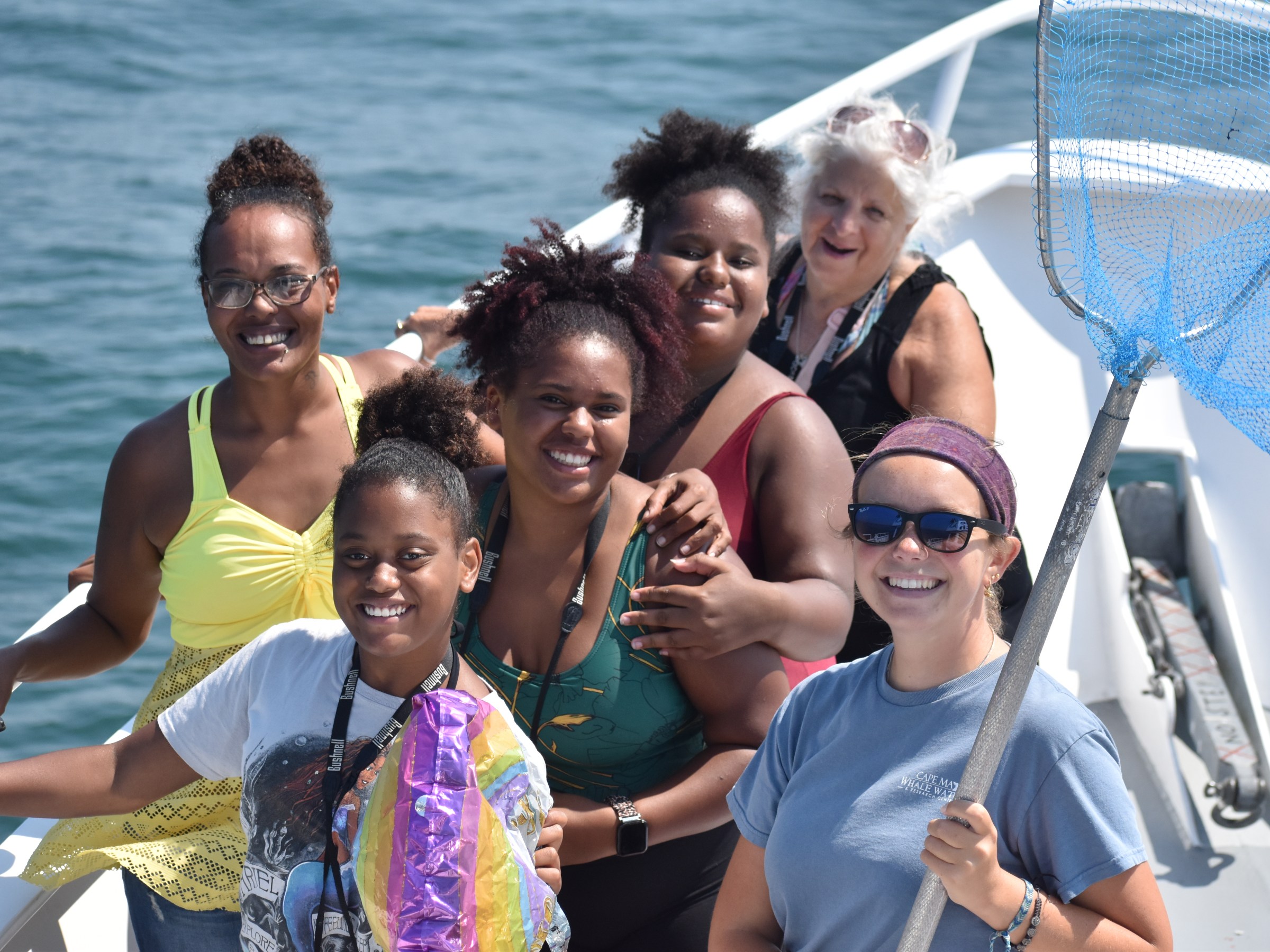 Group of six people smiling on a boat with the ocean in the background.