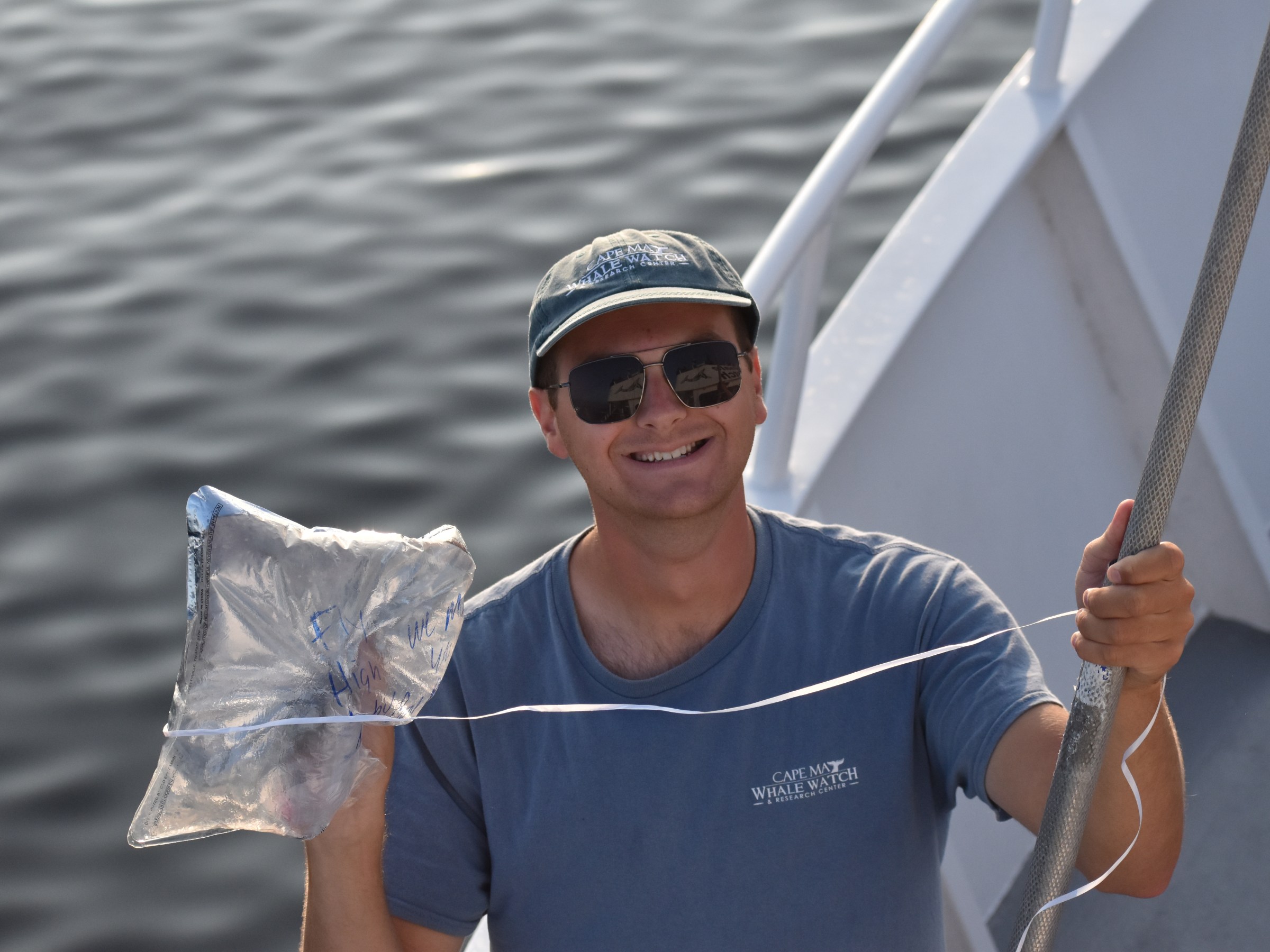 Person on a boat holding a shiny bag, wearing a cap and sunglasses.