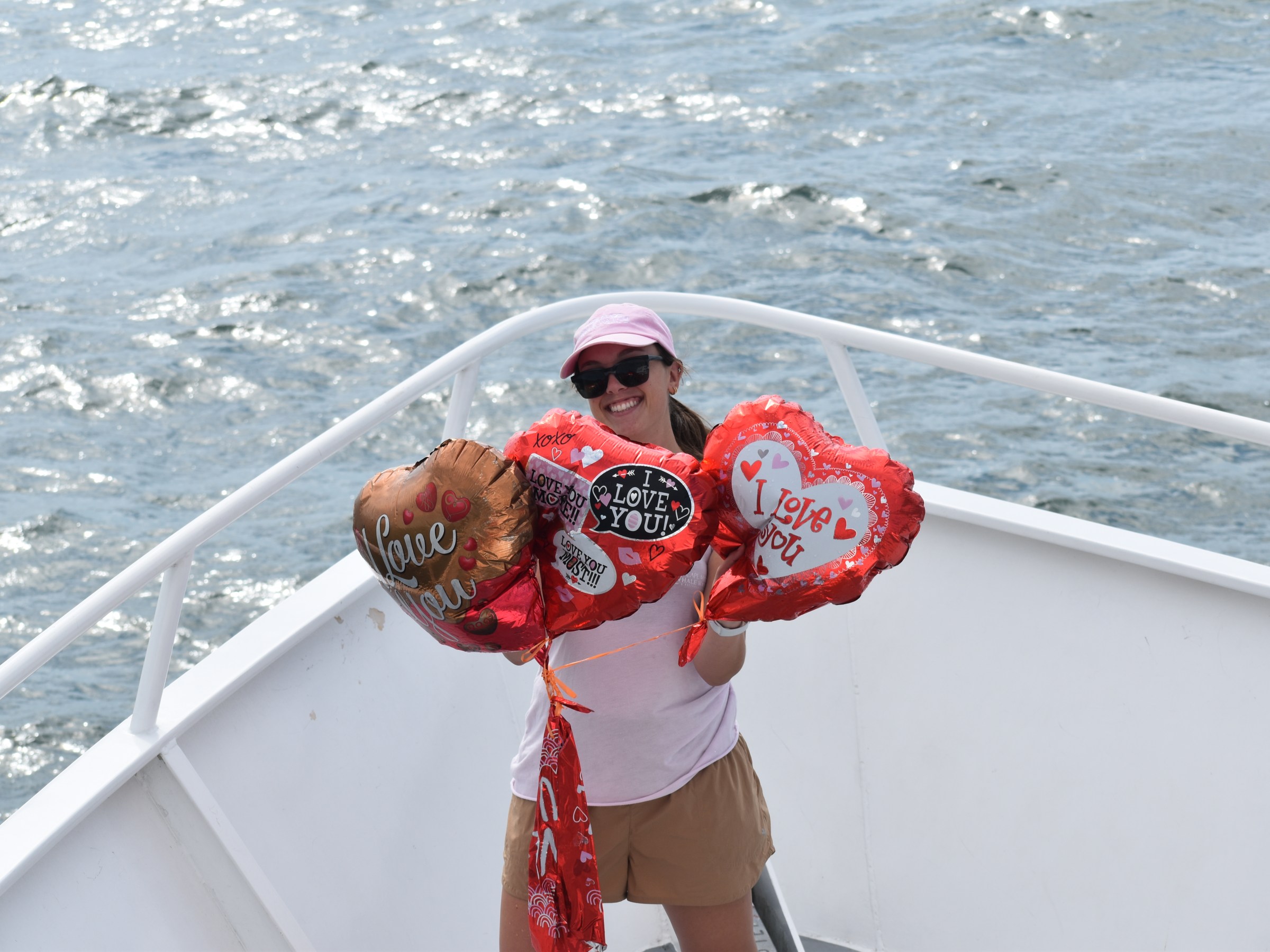 Person on boat holding heart-shaped balloons with 'I love you' text.